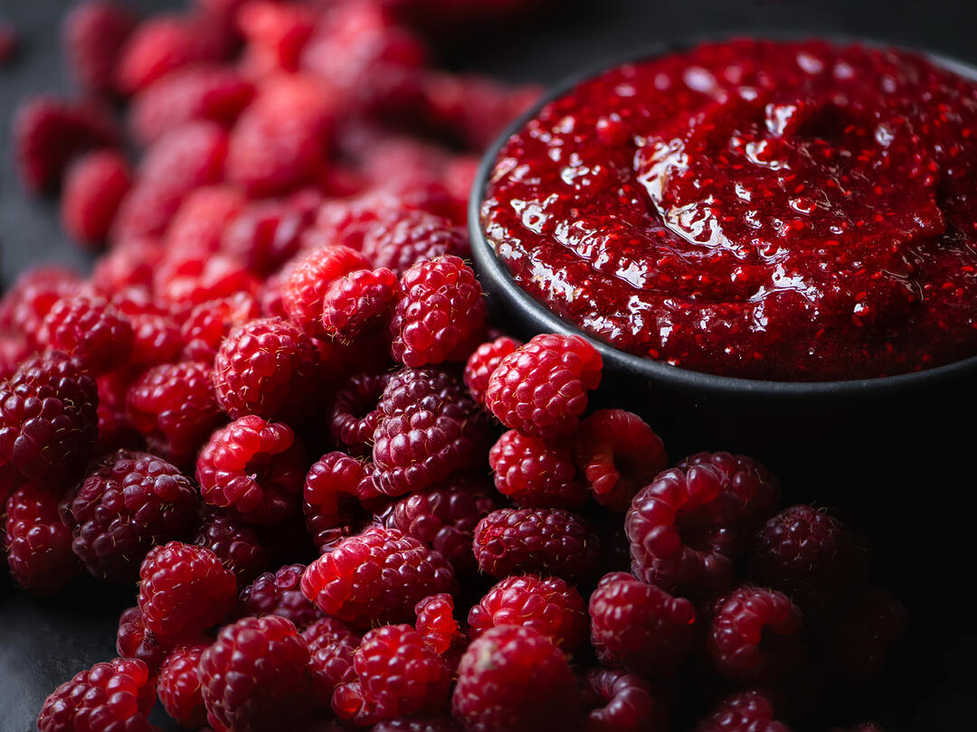 Bowl of raspberry jam alongside fresh raspberries.
